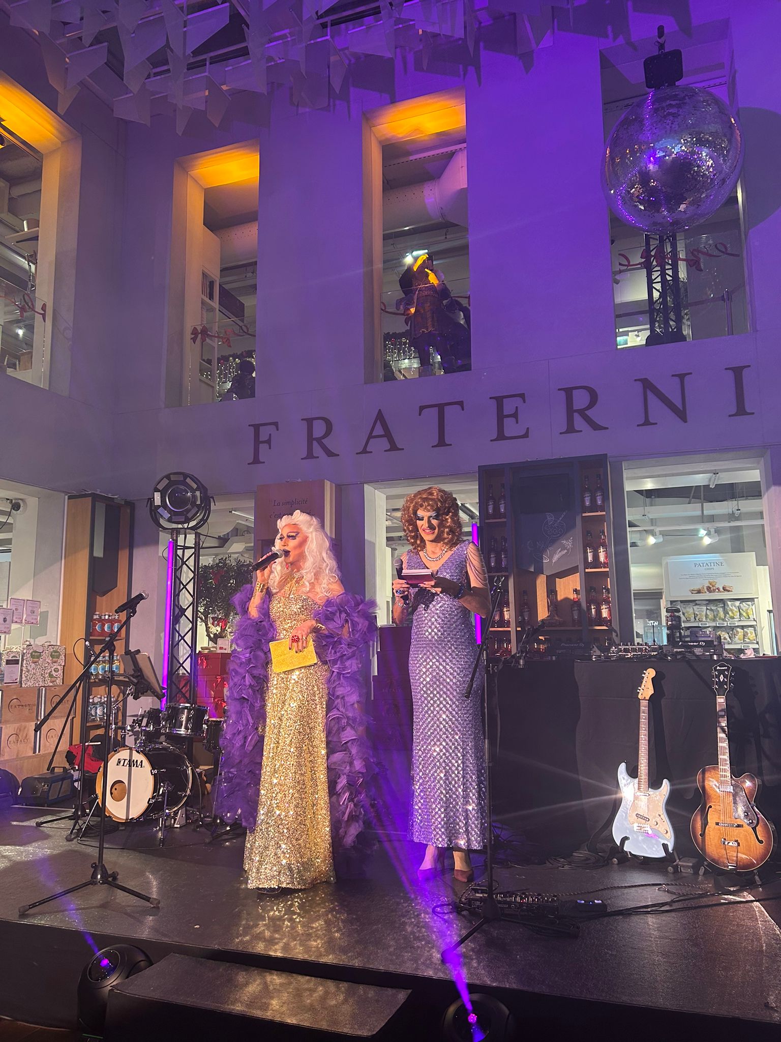 Deux drag queens en robes pailletées et boas sur scène avec instruments à Eataly Paris
