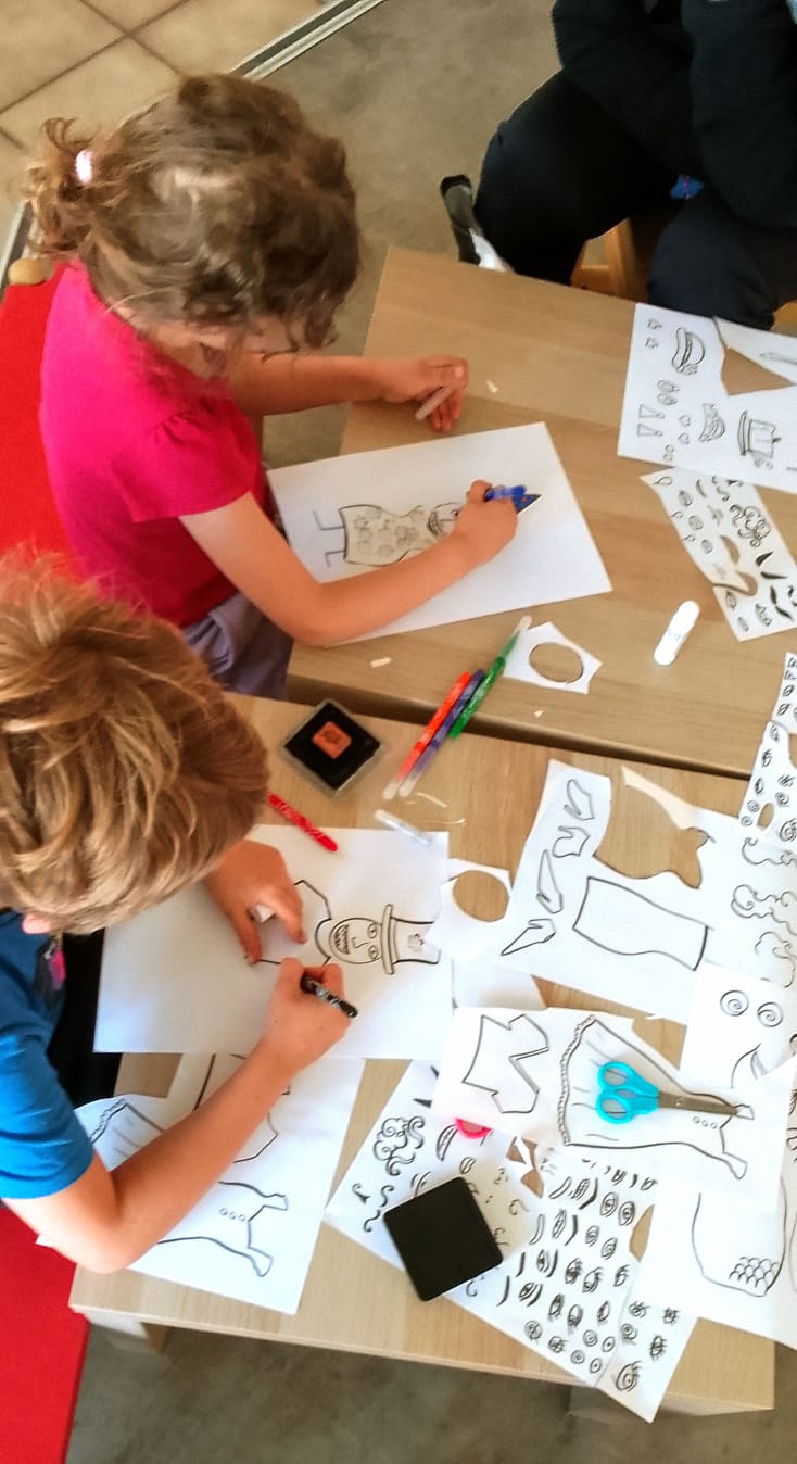 Deux enfants réalisent des personnages sur papier, entourés de formes découpées